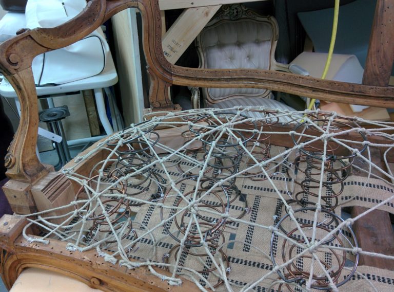 Carved wooden armchair frame with the seat stripped to springs, twine and webbing