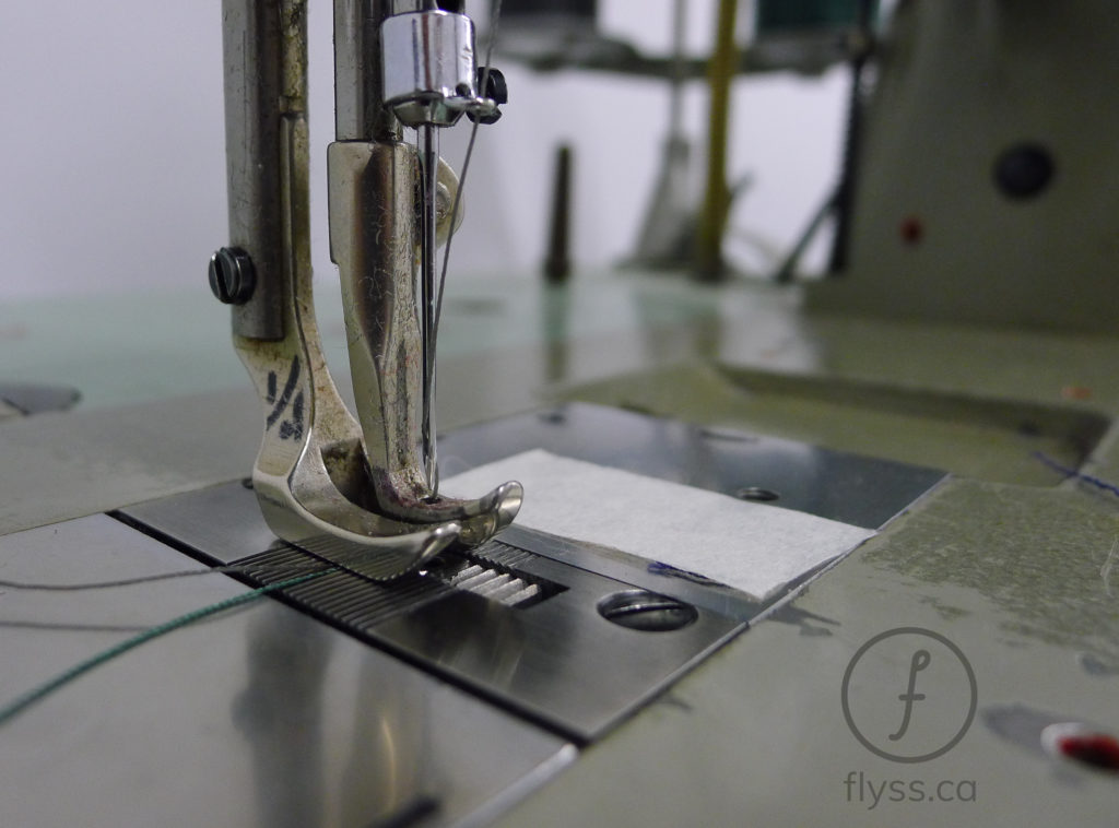 Close-up of a sewing machine presser foot and needle over a small piece of white fabric